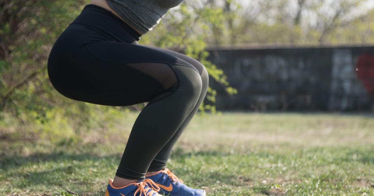 Woman in black leggings holding a bodyweight squat on the grass in a park